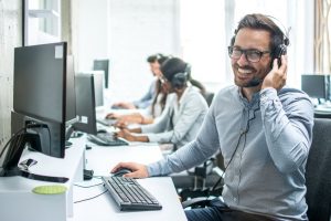 Man sitting at his desk smiling with a headset on his computer