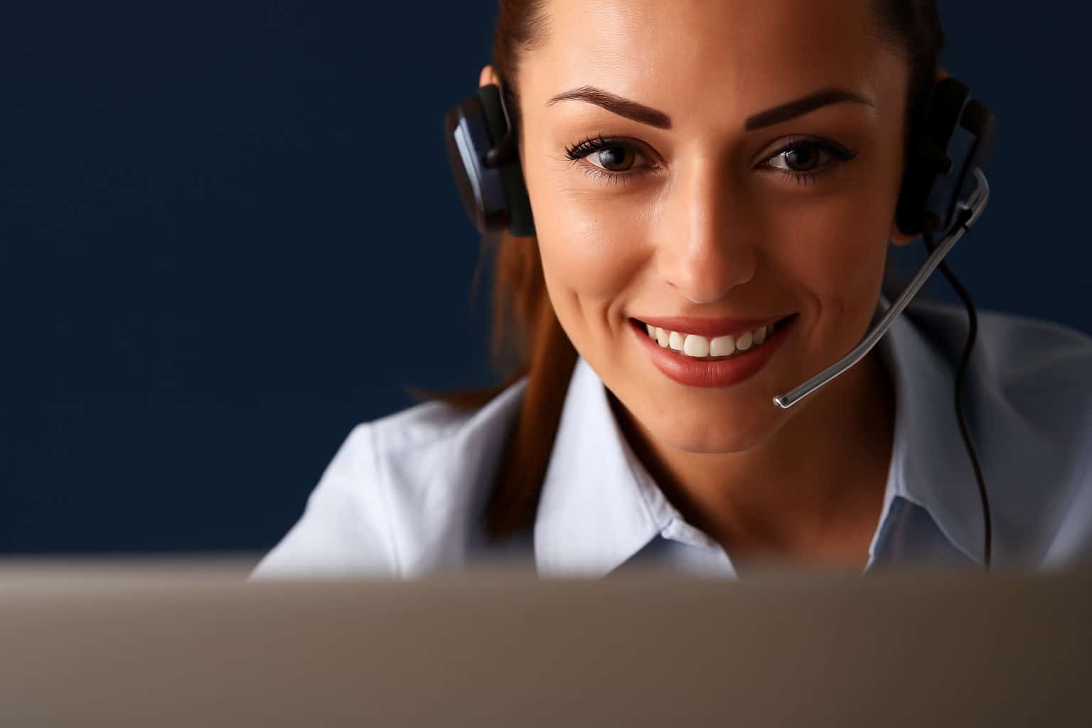 Close-up of smiling woman wearing a headset at work on laptop